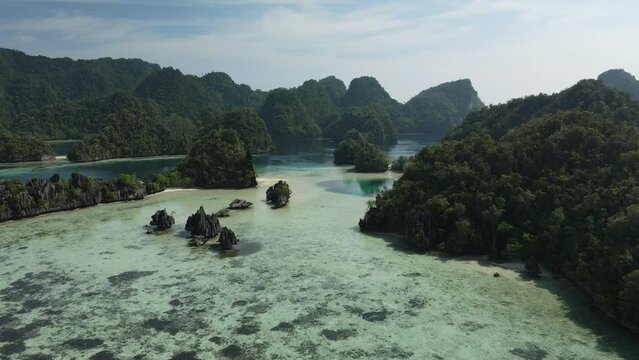aerial shoot, flight over colourful lagoon with Turquoise water, sand beach and palm trees in Raja Ampat Indonesia