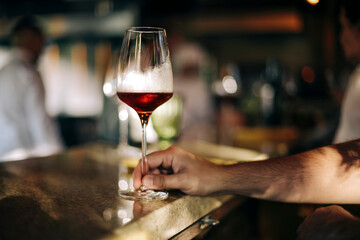 Man holding a glass of red wine in a restaurant or cafe on a wooden table in front of the window