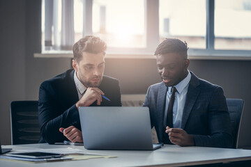 Two confident businessmen in formalwear looking at laptop while working in the office together