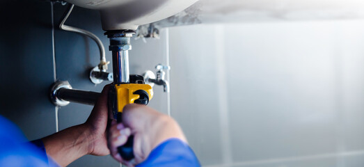 Plumber fixing white sink pipe with adjustable wrench.