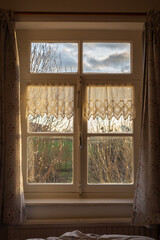 View of the natural countryside through an old-fashioned window with net curtains on the sides.