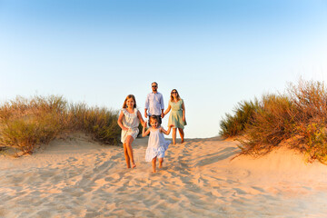 Happy family young parents two kids walking on sandy beach on sunny day during summer vacation