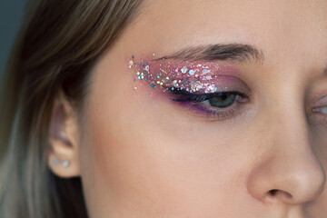 Close up of a young caucasian woman with purple and pink eye shadow and glitter on the eyelids. Party, holiday festive makeup - obrazy, fototapety, plakaty