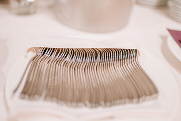 close-up of neatly arranged silver forks on a white tablecloth, part of a table setting for a...