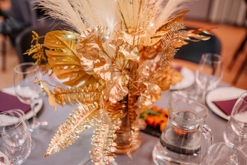 close-up of a golden floral centerpiece on an event table, with glassware and a blurred background of the venue.