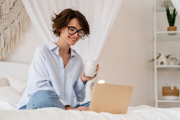 pretty young woman working online remote at home in bedroom sitting on bed using laptop