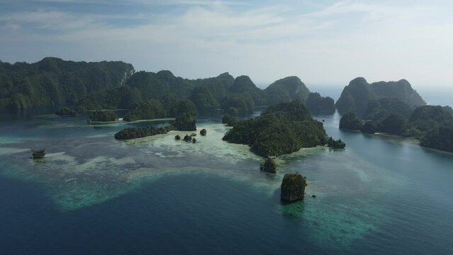 aerial shoot, flight over colourful lagoon with Turquoise water, sand beach and palm trees in Raja Ampat Indonesia