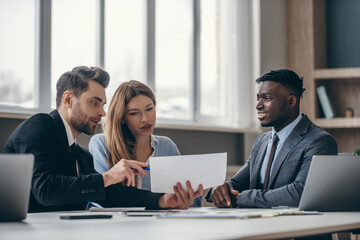 Young couple sitting at the office desk and examining papers while visiting financial advisor