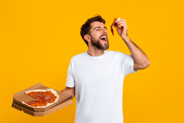 Man Eating Pizza Holding Pizzeria Box Over Yellow Studio Backdrop