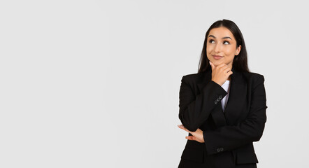 Cheerful pensive businesswoman in suit thinking, looking at empty space, isolated on gray background studio background