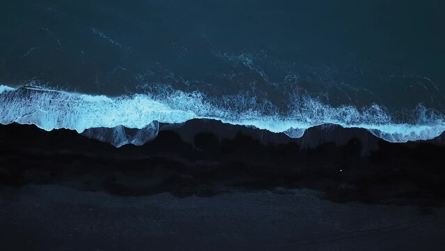 Stunning view of cold ocean waves lapping black volcanic sand beach, aerial directly above shot. Concepts of nature power and natural pattern background.