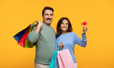 A joyful couple with a man holding colorful shopping bags and a woman holding a red credit card