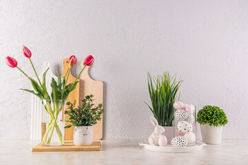 Beautiful festive decoration of the kitchen countertop for Easter Day. vase with tulip, green plants, eggs with pattern in high glass, easter bunnies.