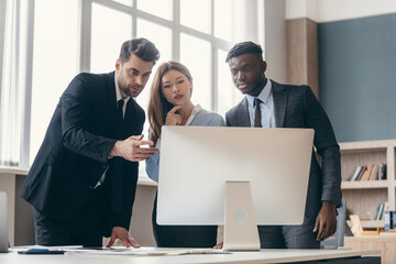 Three confident business people analyzing data while pointing computer monitor in office