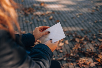 Woman opens a white envelope with a letter. Autumn foliage in the background.