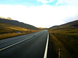 Droga asfaltowa rozciąga się pomiędzy górami. Górska droga znajdująca się na Wyspach Owczych. Surowy klimat widoczny w oddali. - obrazy, fototapety, plakaty