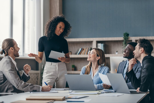 Group of young business people listening to a female speaker while sitting at the office desk