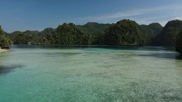 aerial shoot, flight over colourful lagoon with Turquoise water, sand beach and palm trees in Raja Ampat Indonesia