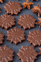 Chocolate candies in the shape of snowflakes. Brown food background.