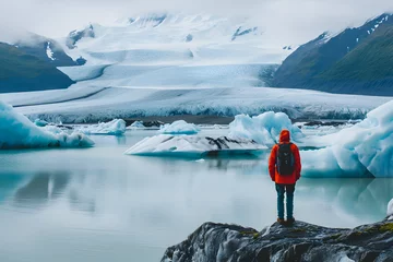 Zelfklevend Fotobehang A man-mountaineer in a red jacket stands on a rock and looks at the frozen glaciers and the frozen ocean. © Jovana Arandjelovic