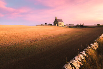 The lone chapel Boarhills Church during a colourful sunset or sunrise in the rural countryside farmland of East Neuk, Fife, Scotland, UK.