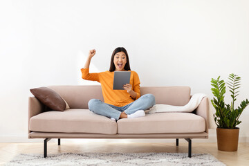 Smiling asian lady holding digital tablet, gesturing, home interior