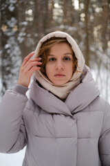 A young woman stands against a background of fir trees under a snowy forest in winter. A girl in a...