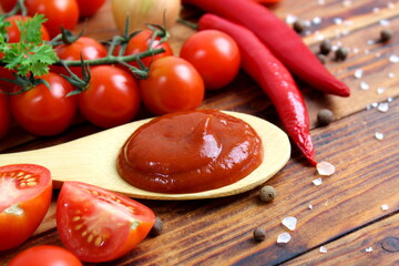 There are vegetables and a spoon with tomato paste on a wooden table.