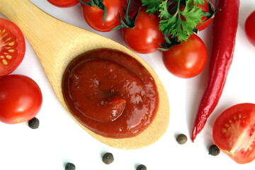 A wooden spoon with tomato sauce and vegetables lies on a white background.