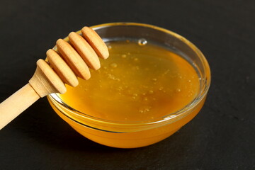 On a black background there is a glass plate with fresh honey and a special spoon.