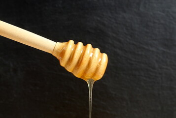 Fresh transparent honey flows from a wooden ladle.