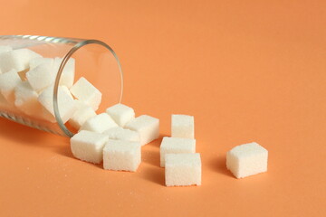 A glass glass with pieces of refined sugar lies on an orange background.
