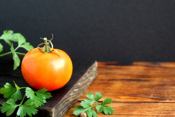 There is a black cutting board with a yellow tomato on a wooden table.	