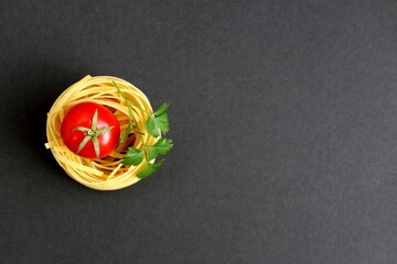 On a black background lies one nest of spaghetti with a red tomato.