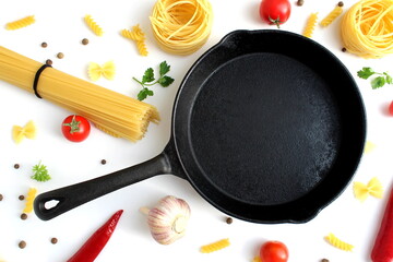 A cast iron frying pan lies on a white background surrounded by vegetables and dry pasta