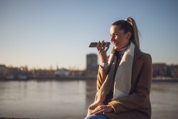 Beautiful woman in warm clothing talking on a mobile phone and enjoys resting by the river on a...