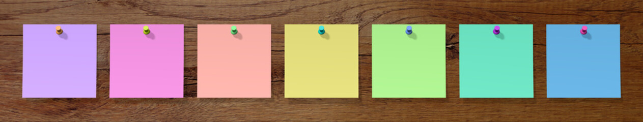 sieben leere bunte Notizzettel auf ein Holzbrett gesteckt