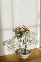 Beautiful pink and white flowers in bowl on rustic background. Tender floral composition on kenzan or flower pin in sunlight. Modern flower arrangement