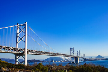 The Seto Ohashi Bridge spans the calm Seto Inland Sea in Japan under a clear blue sky, connecting Okayama and Kagawa with a dual car and train route.