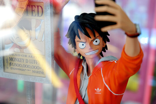 Pirate Monkey D. Luffy, of Japanese manga series One Piece, wanted by the authorities, coolly takes a selfie with a 'Dead or Alive' poster of himself. Toy merchandise at a shop window display.