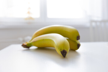 yellow bananas placed on a white table and in the background a window with a chair in the kitchen.