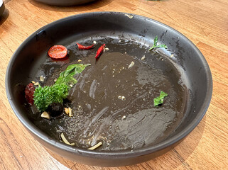 Empty black plate from eating spicy spaghetti bacon. There are food scraps left on the plate such as dried chilies, olives, tomatoes, garlic, basil leaves, and spaghetti.