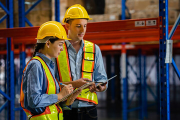 engineers taking notes using tablets in a large industrial warehouse. Workers in safety clothing...