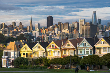 Painted sisters in San Francisco with the city skyline at sunset, skyscrapers of different colors, dramatic sky.	