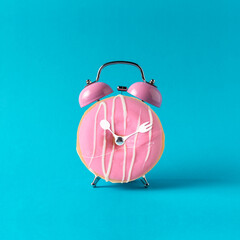 Pink alarm clock donut on pastel blue background. Minimal concept.