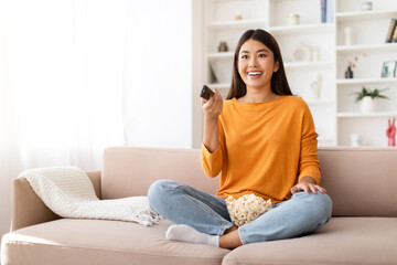 Happy young chinese lady enjoying time at home, watching TV