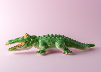 Green crocodile toy on pastel pink background. Minimal art concept.