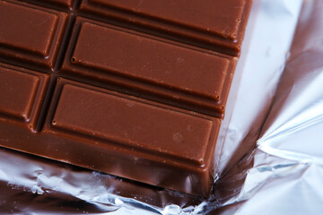 Bar milk chocolate lies on foil.