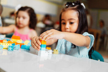 Little female children playing with colored blocks. - obrazy, fototapety, plakaty