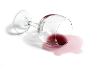 An overturned glass of red wine lies on a white background.